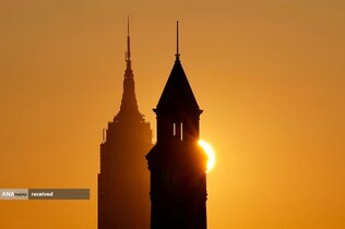 منظره خورشید از پشت ساختمان امپایر استیت در شهر نیویورک و برج ساعت لاکوانا در هوبوکن، نیوجرسی